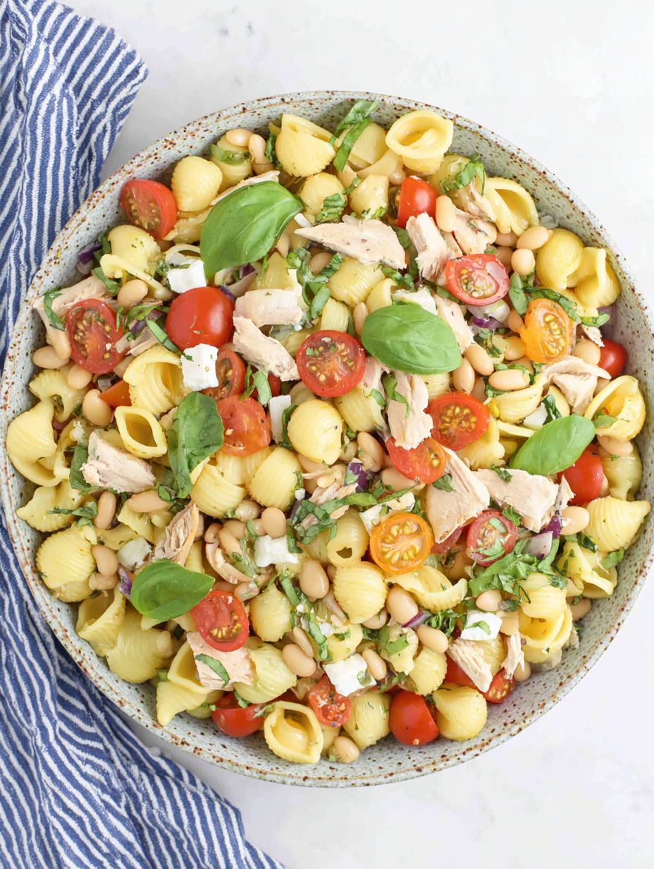 A bowl of pasta salad with chicken, tomatoes, beans, and spinach.