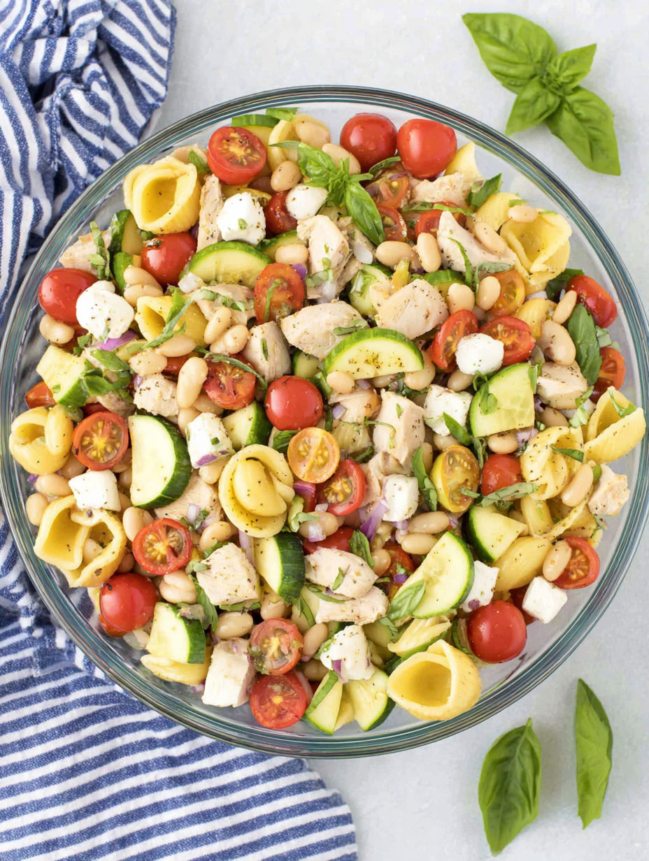 A bowl of pasta salad with chicken, tomatoes, zucchini, and beans.