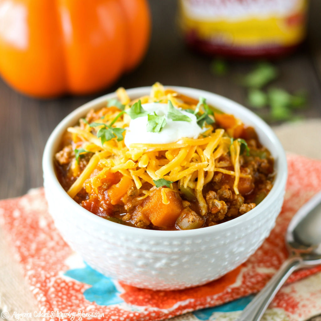 A bowl of chili with cheese and chives on top.