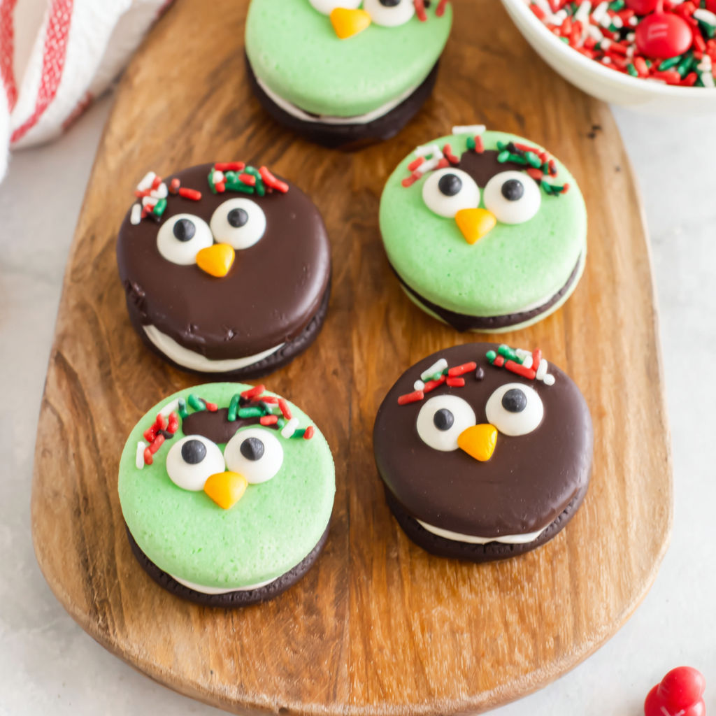A wooden cutting board with four green and black penguin cookies.