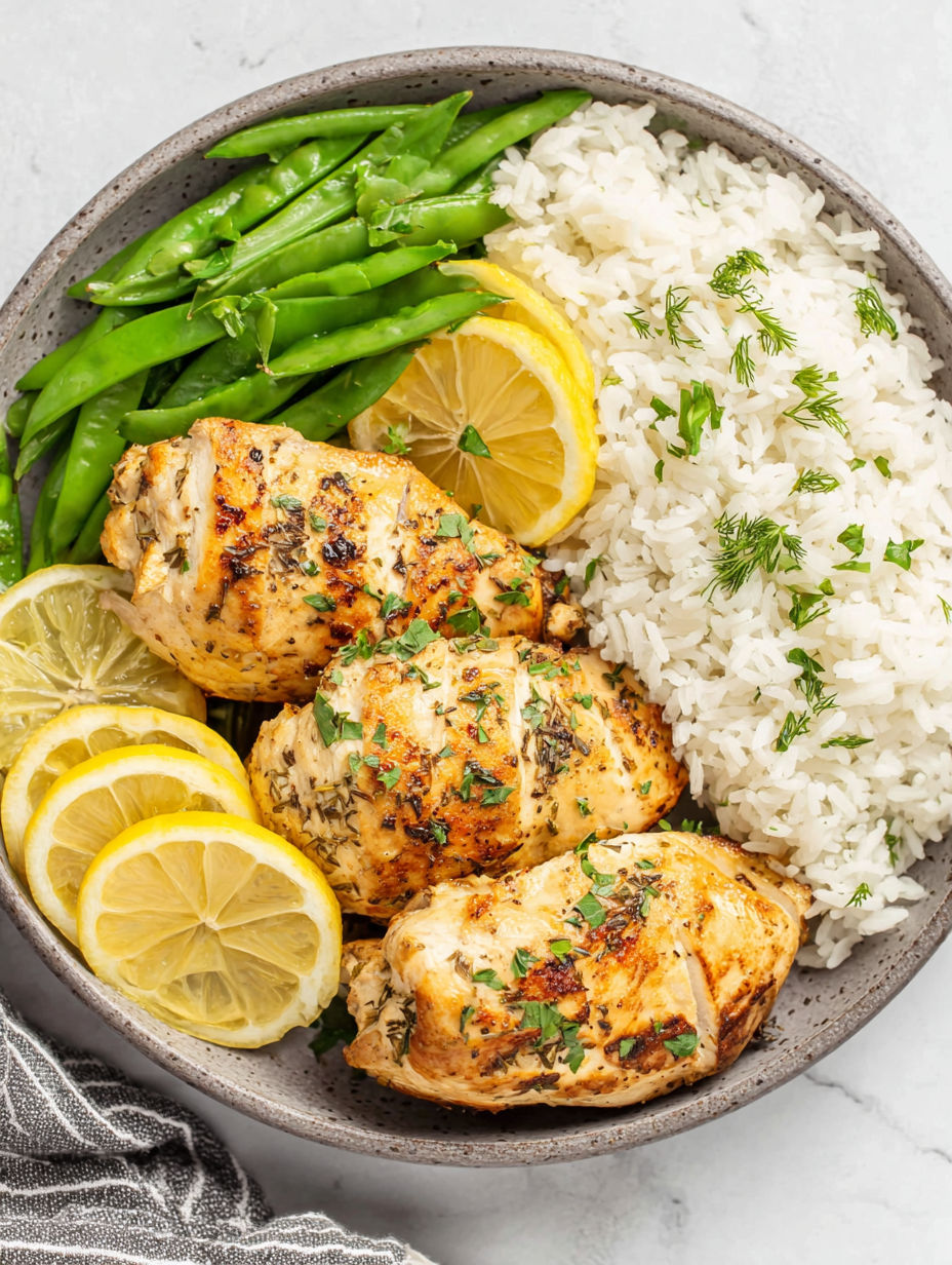 A bowl of food with rice, chicken, green beans, and lemon wedges.