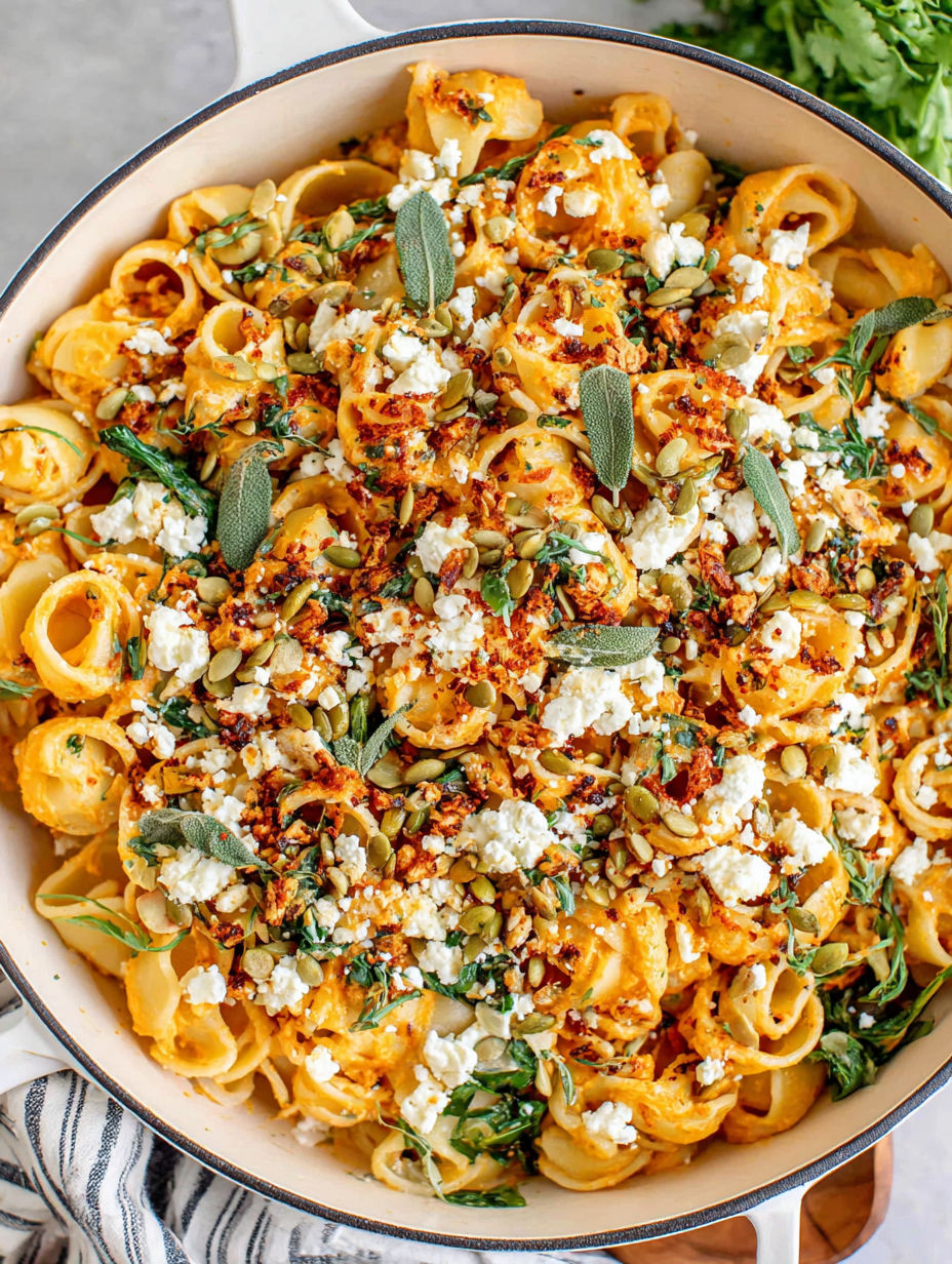 A bowl of pasta with feta cheese and pumpkin seeds.