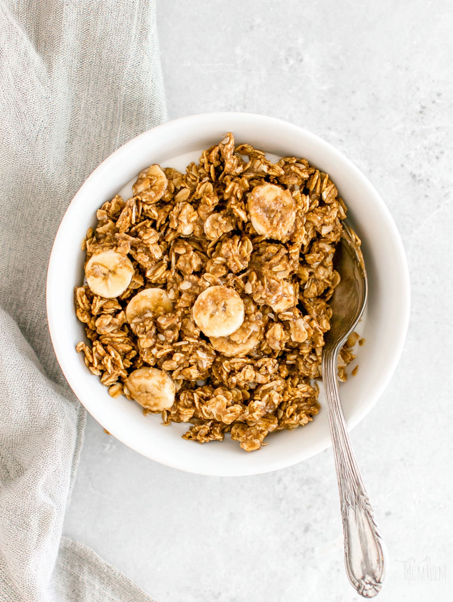 A bowl of granola with bananas and a spoon.