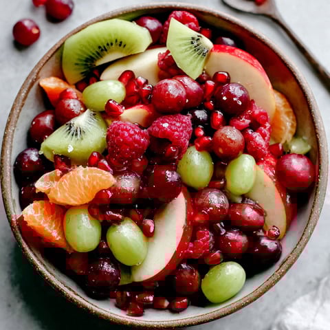 A bowl of fruit salad with kiwi, apples, oranges, and pomegranates.