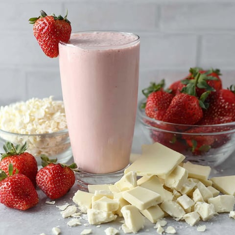 A glass of white chocolate smoothie with strawberries on top.