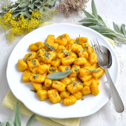 A plate of gnocchi with pumpkin and herbs.