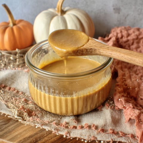 A wooden table with a glass bowl of pumpkin pie sauce.