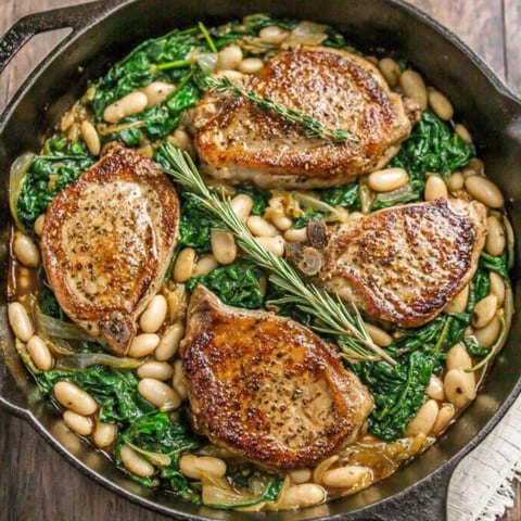 A skillet dinner with pork chops, white beans, and spinach.