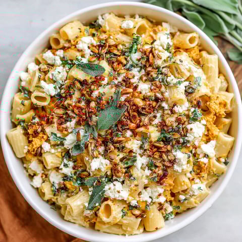 A bowl of pasta with feta cheese and pumpkin seeds.