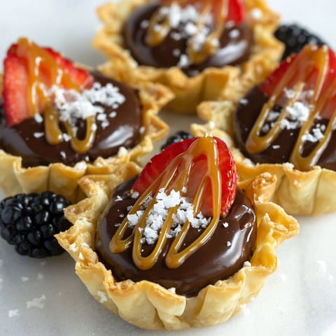 Four mini chocolate ganache tarts with strawberries on top.