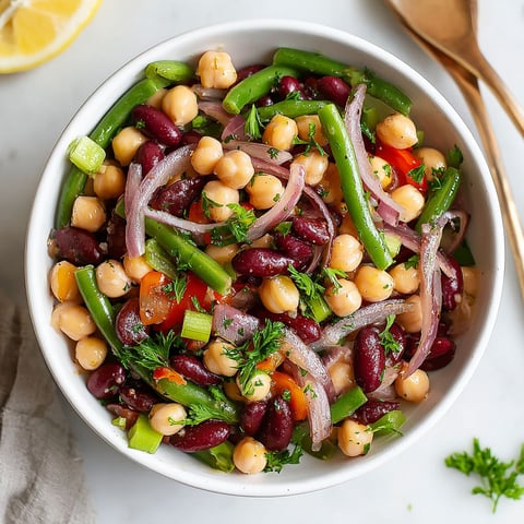 A bowl of three bean salad with green onions and lemon wedges.