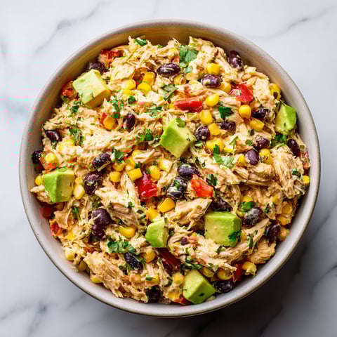 A bowl of chicken salad with avocado, corn, and tomatoes.